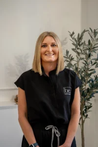 Emma stood in front of plain wall with a plant behind her in the be laser skin clinic in taunton